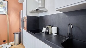 A modern kitchen with a black countertop, a stainless steel range hood, a sink, and a trash can. - Charming new Flat in the Centre of Paris (Paris)