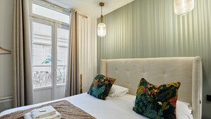 A hotel room with a large bed, two decorative pillows, a hanging light fixture, and a view of bicycles outside the window. - Charming new Flat in the Centre of Paris (Paris)
