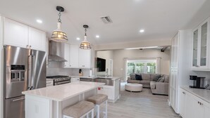 A modern kitchen with stainless steel appliances, a central island with stools, and pendant lighting.