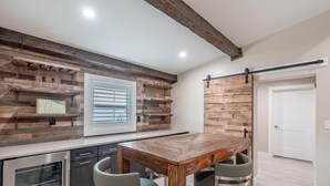 A kitchen with a wooden table and bar stools, a built-in oven, and a window with blinds.