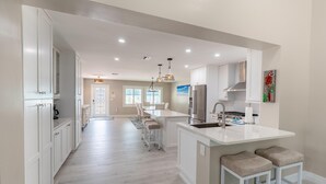 A spacious kitchen with white cabinetry, a central island with stools, and a dining area with chairs.