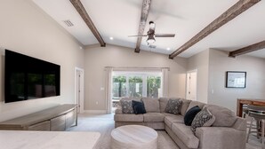 A spacious living room with a large sectional sofa, a round ottoman, a flat-screen TV, and a ceiling fan.