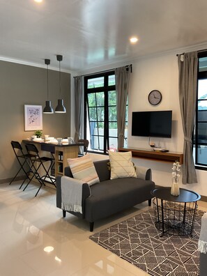 Un soggiorno moderno con un divano, un tavolino e una TV. Si nota una zona pranzo con sedie e un tavolo, e una cucina sullo sfondo.