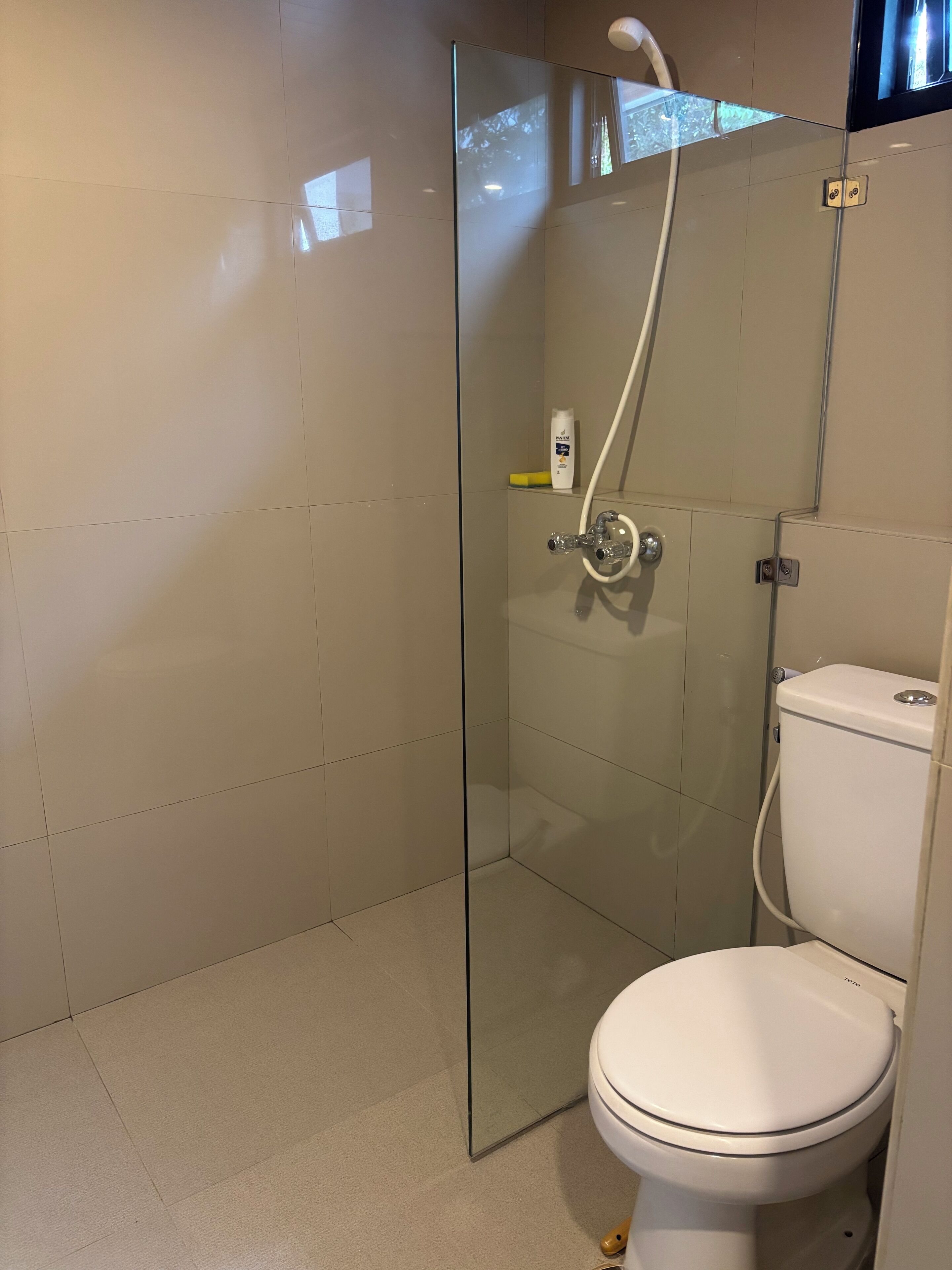 A modern bathroom with a glass shower enclosure, a toilet, and a visible hand dryer.