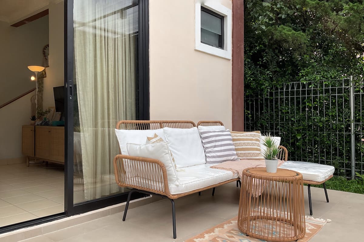 A wicker sofa with cushions, a small round table, and a potted plant on a tiled patio.