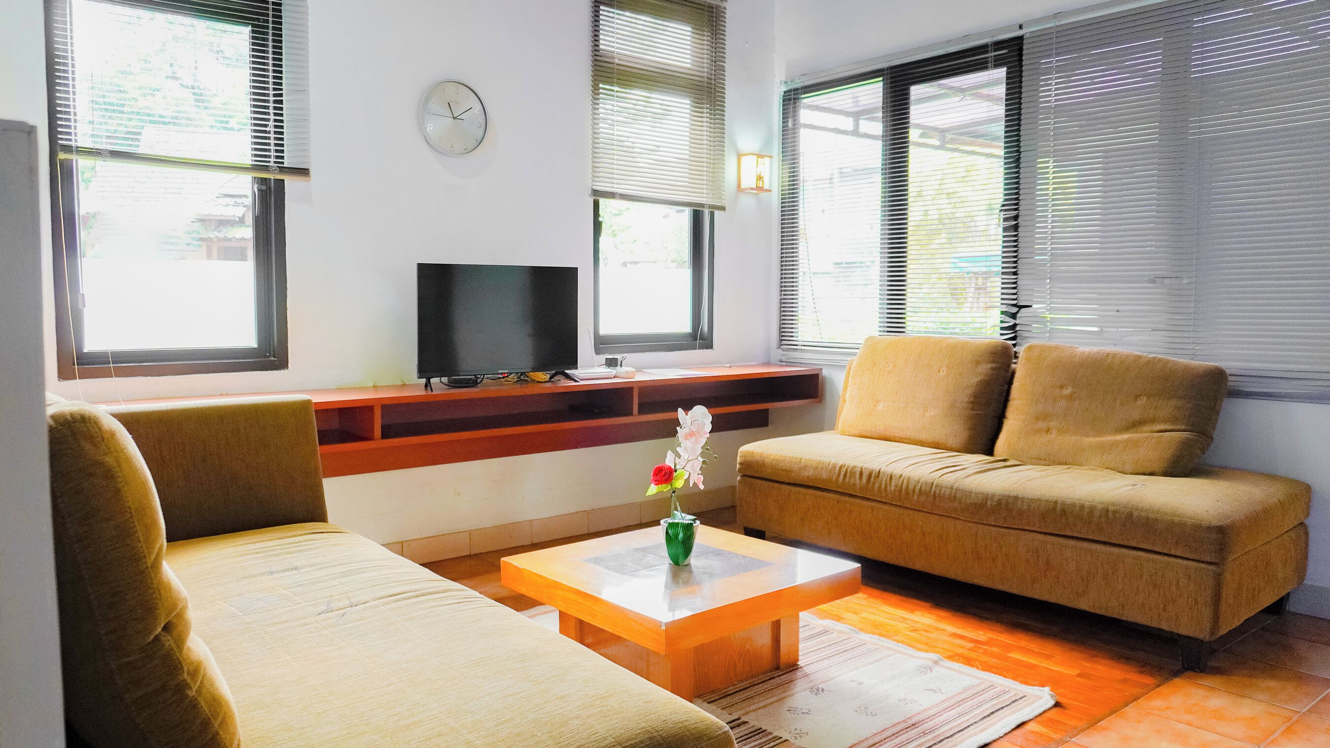 A living room with a sofa, armchair, coffee table, TV, and a clock on the wall.