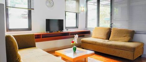 A living room with a sofa, armchair, coffee table, TV, and a clock on the wall.