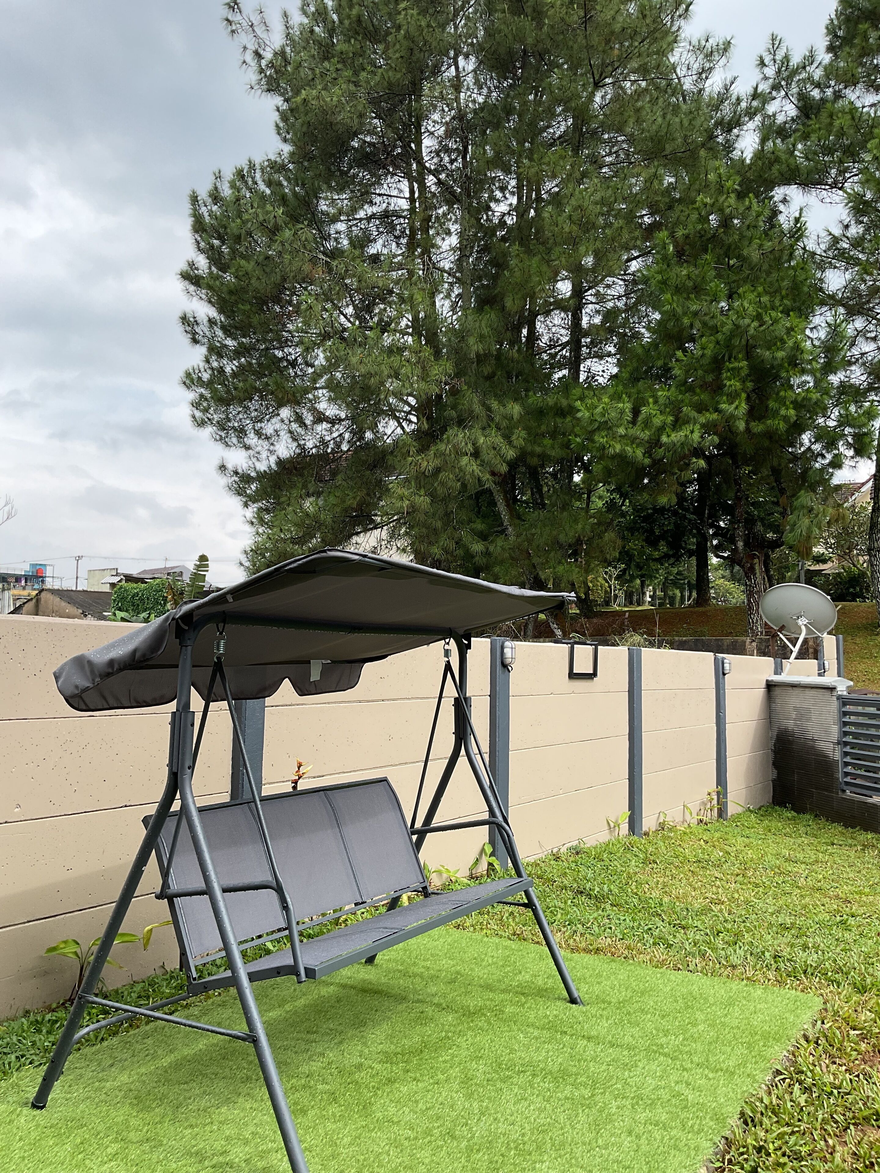 A camping chair with a canopy, positioned on artificial grass near a concrete wall with a satellite dish.