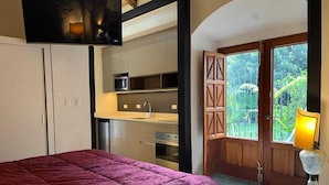 Une chambre avec un grand lit, un coin cuisine et un balcon donnant sur un espace verdoyant.