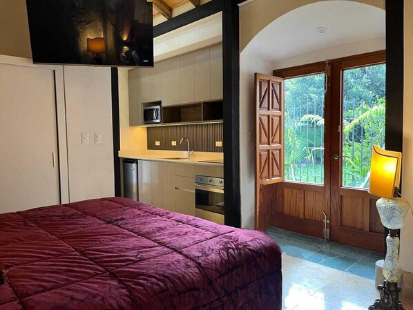 Un dormitorio con una cama grande, kitchenette y un balcón con vistas a zonas verdes.