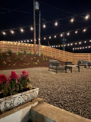 Un patio con cerco de madera, luces colgantes y mobiliario exterior.