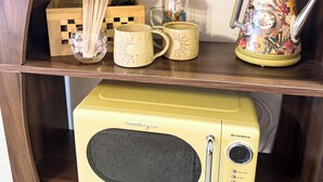 A retro-style microwave on a wooden shelf, a floral teapot, and two matching mugs with a checkered box and wooden utensils.