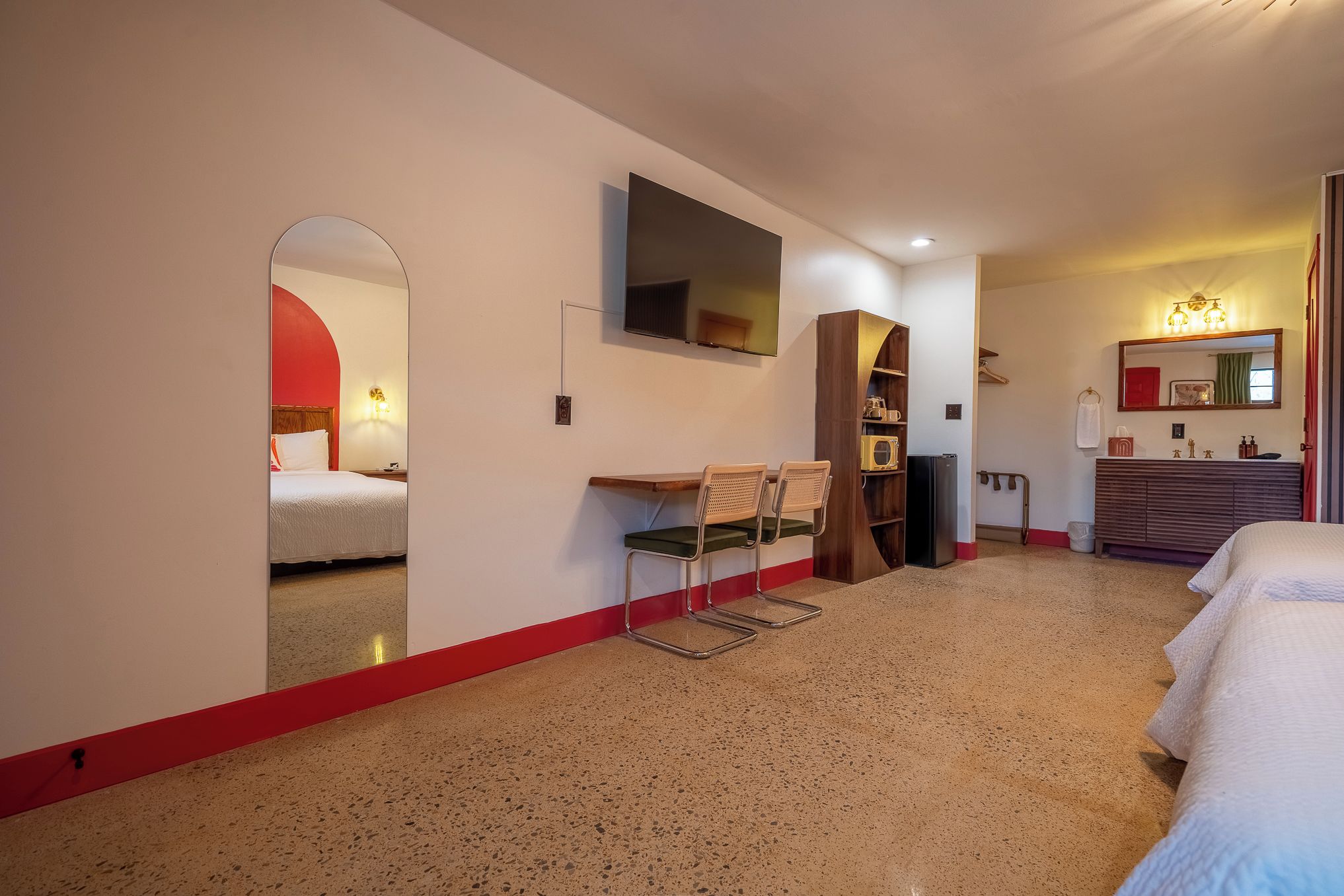 Ein Hotelzimmer mit einem Bett, einem Schreibtisch mit zwei Stühlen, einem Fernseher, einem Kleiderschrank und einem Badezimmer mit Spiegel und Waschbecken.