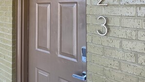 A brown door with a keypad lock, a brick wall with numbers 1, 2, and 3, and a small window above the door.