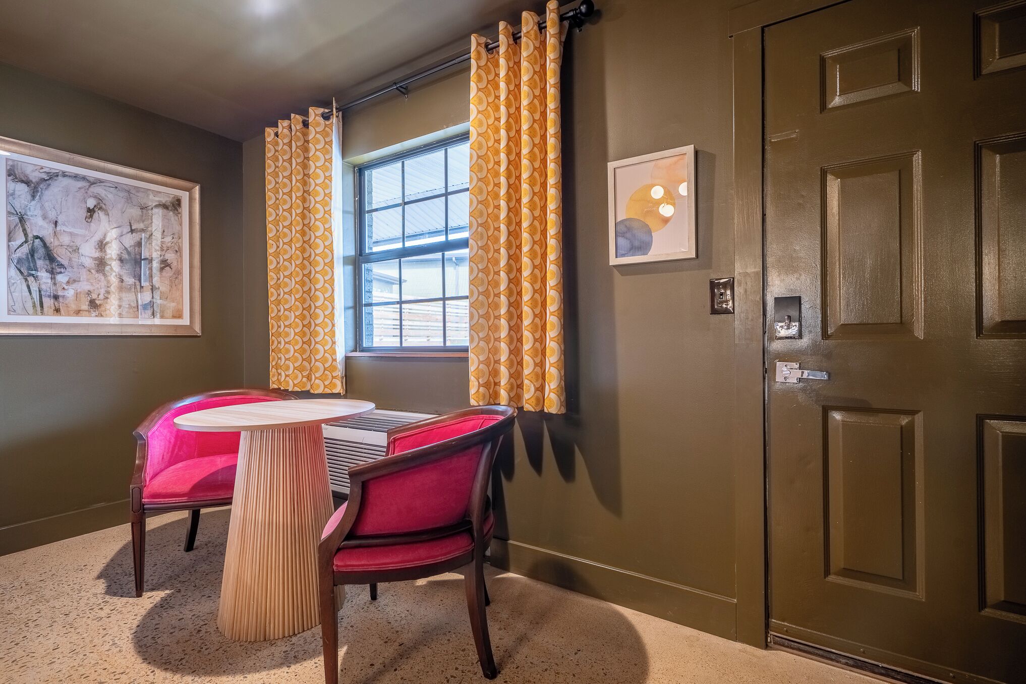 A room with a dining table, chairs, a window with curtains, a door, and artwork on the walls.