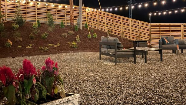 Un patio con cerco de madera, luces colgantes y mobiliario exterior.