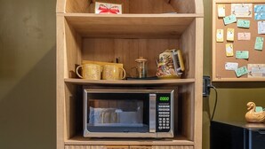 A wooden cabinet with a microwave, a corkboard with notes, and a swan figurine.