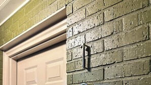 Una puerta blanca con un muro de ladrillo verde y dos números de casa metálicos.