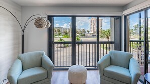 Ein modernes Wohnzimmer mit zwei Sesseln, einem runden Hocker und einem großen Fenster mit Blick auf eine Skyline und Palmen.