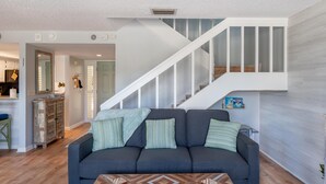 Ein modernes Wohnzimmer mit einem dunkelblauen Sofa, einem Holztisch und einer Treppe mit weißen Geländern, die zu einer oberen Ebene führt.