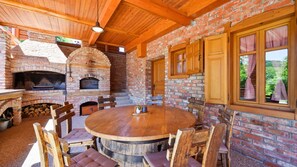 Un espace de restauration extérieur de style rustique, avec une cheminée en briques, des meubles en bois et une vue sur la verdure.