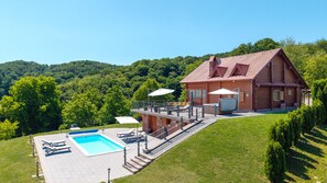 Une cabane en rondins avec une piscine, un espace salon extérieur et une vue panoramique sur une colline.