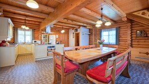 L’intérieur d’une cabane en rondins, avec une table à manger en bois, des chaises, un coin cuisine et une grande fenêtre.