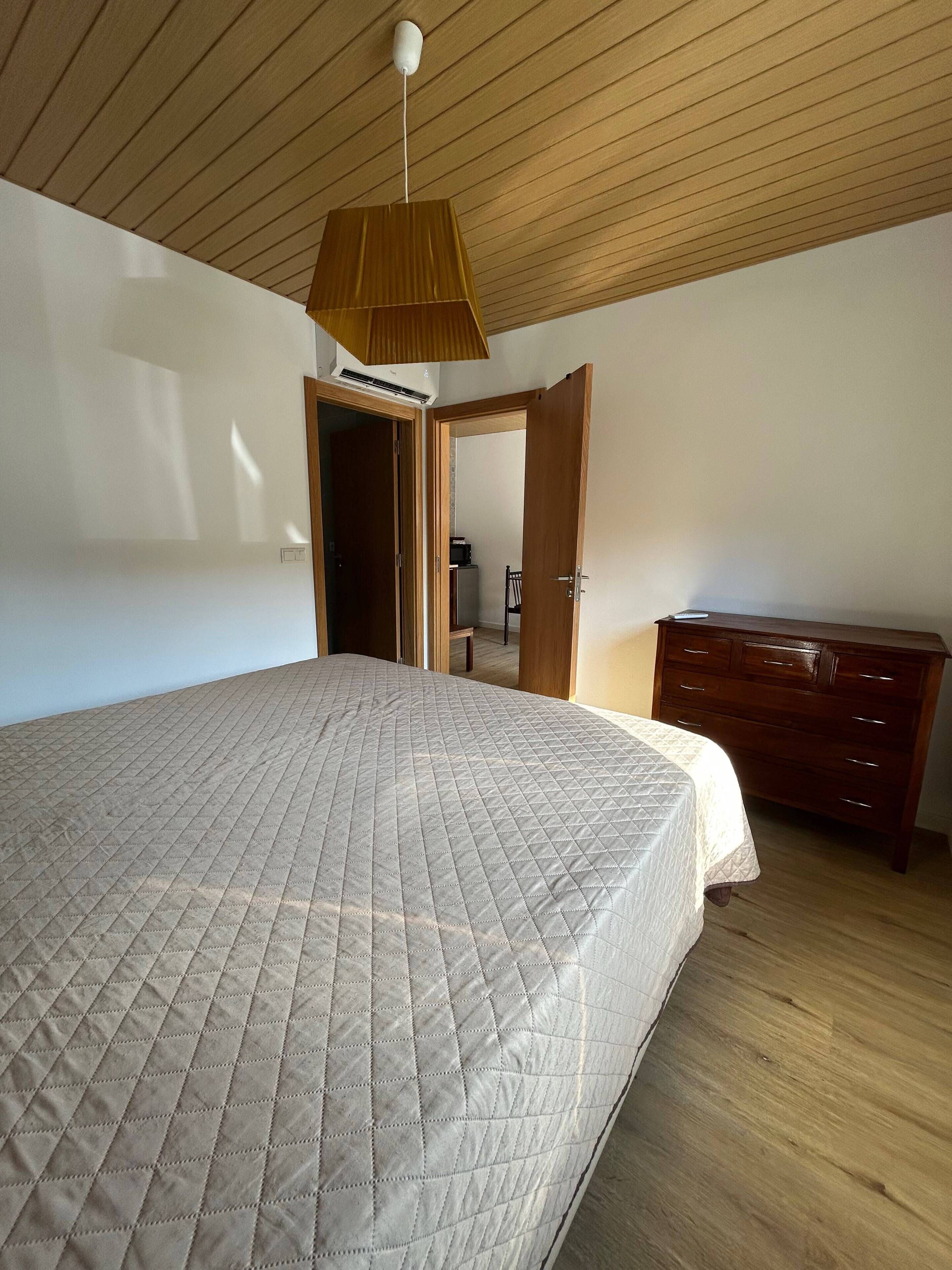 A bedroom with a large bed, wooden ceiling, and a dresser.