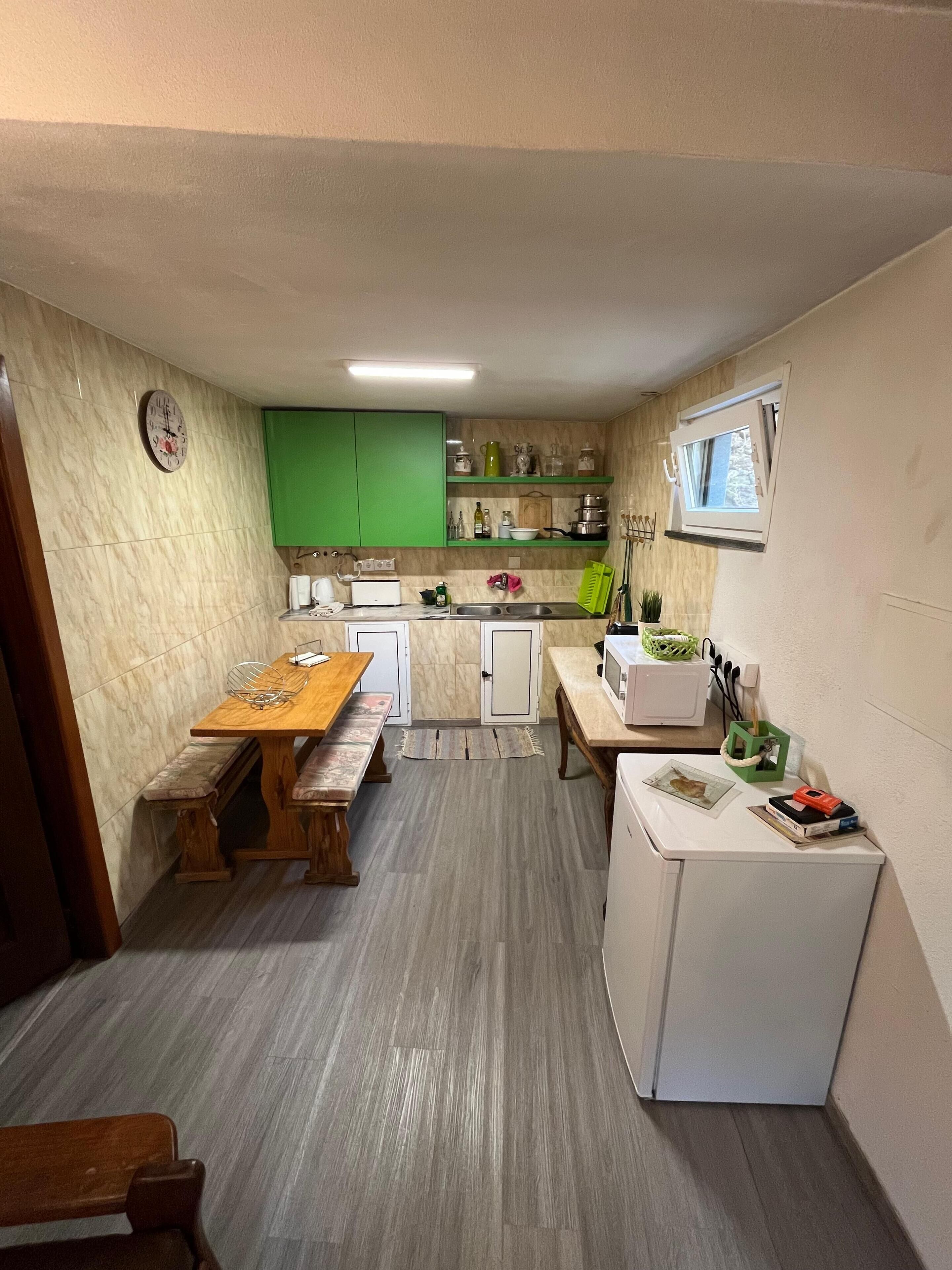 Een kleine keuken met een houten tafel, een bankje, een koelkast en een raam.