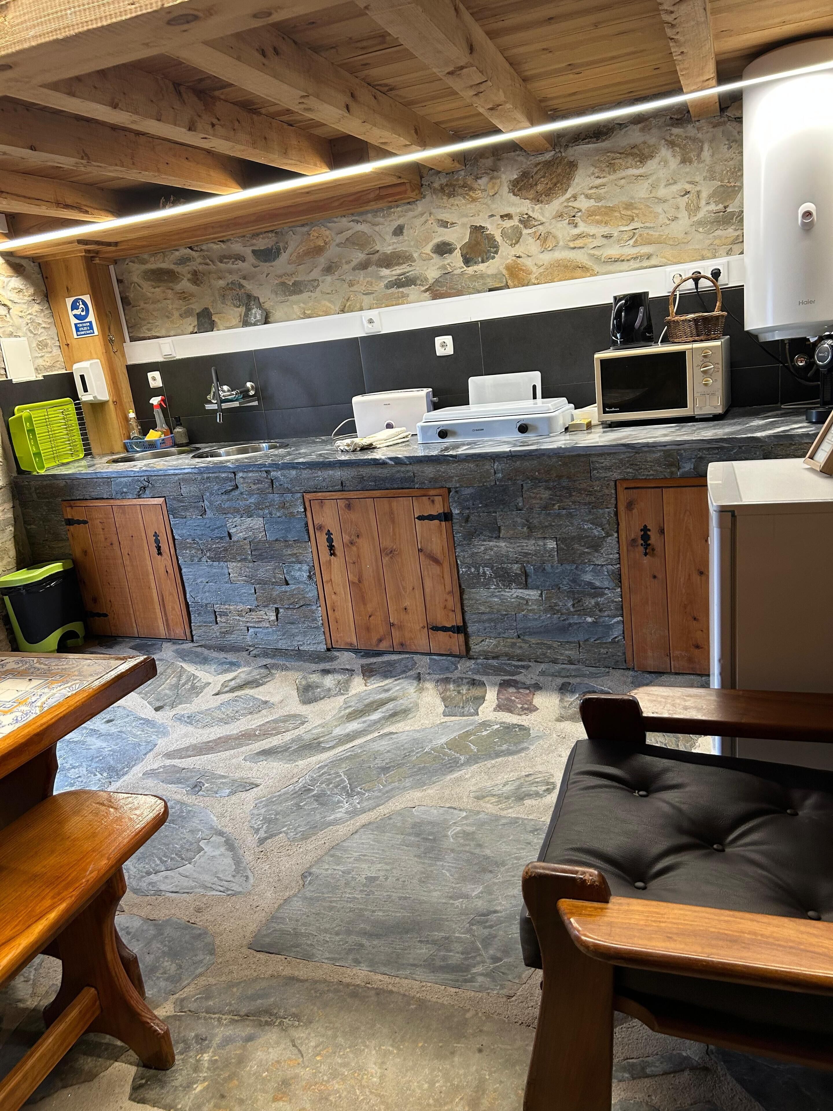 A rustic kitchen with stone walls, wooden beams, and a stone countertop.