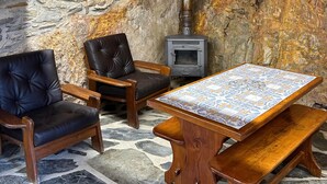 A rustic interior with a stone wall, a wood-burning stove, leather chairs, and a tiled table. - Casas do Sinhel (Góis)