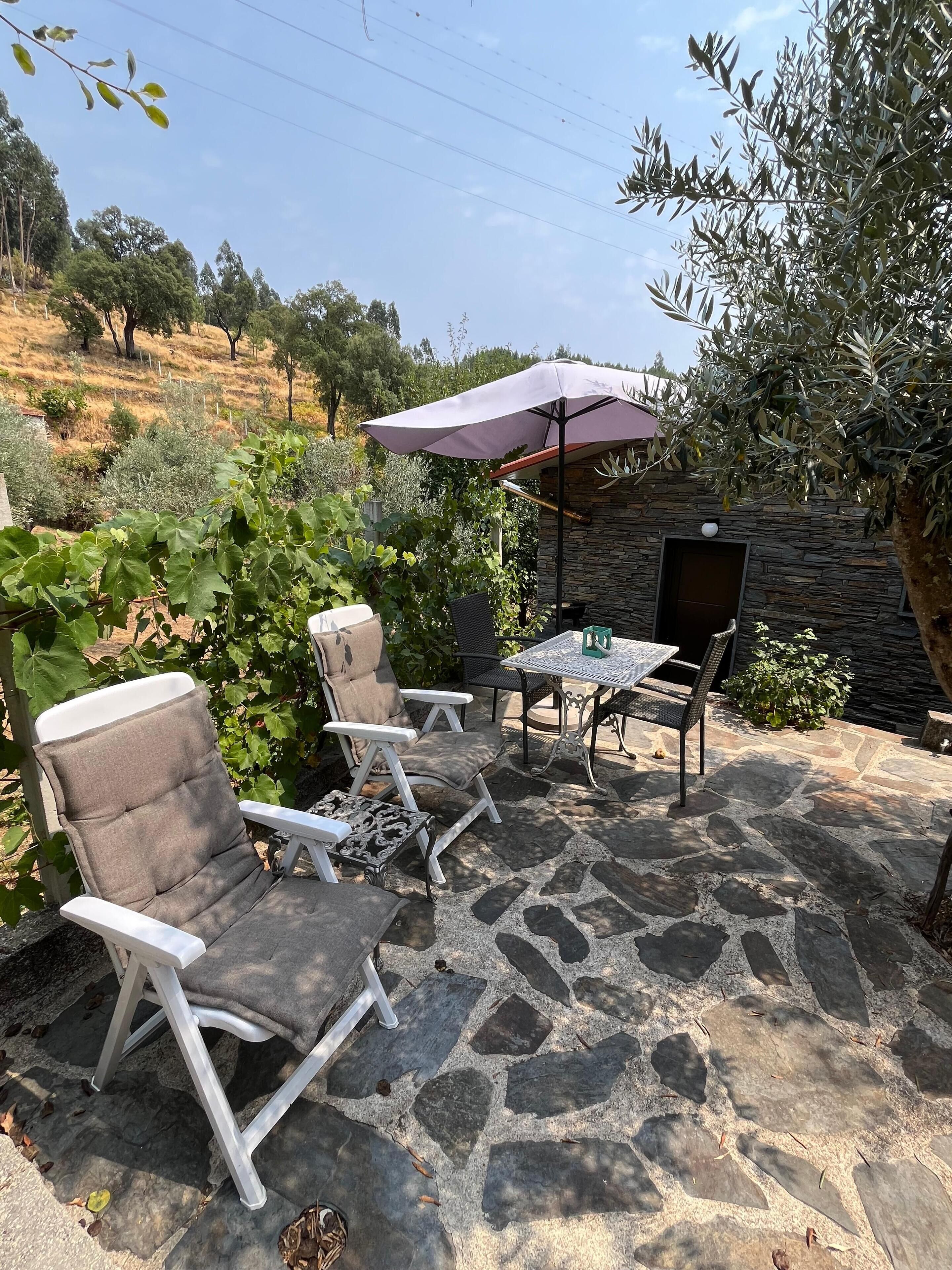 Eine Terrasse im Freien mit Steinboden, einem Tisch, Stühlen und einem Sonnenschirm.