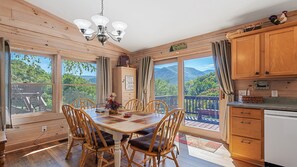 A wooden cabin kitchen with a dining table, chairs, and a view of mountains through large windows. - Mountain Peeks Cabin | Views & Game table (Maggie Valley)