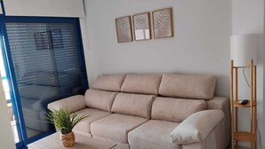 Una sala de estar moderna con un sofá beige, una mesita de centro blanca con una planta y una lámpara de pie de madera.