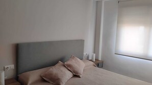 Un dormitorio con cama, dos almohadas, una mesita de noche, una lámpara y una ventana con persianas.