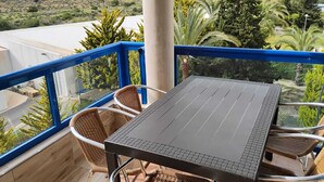 Un balcón con mesa y sillas, con vista a un paisaje montañoso.