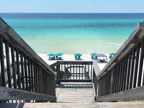 A wooden staircase leading to a beach with turquoise water and umbrellas.