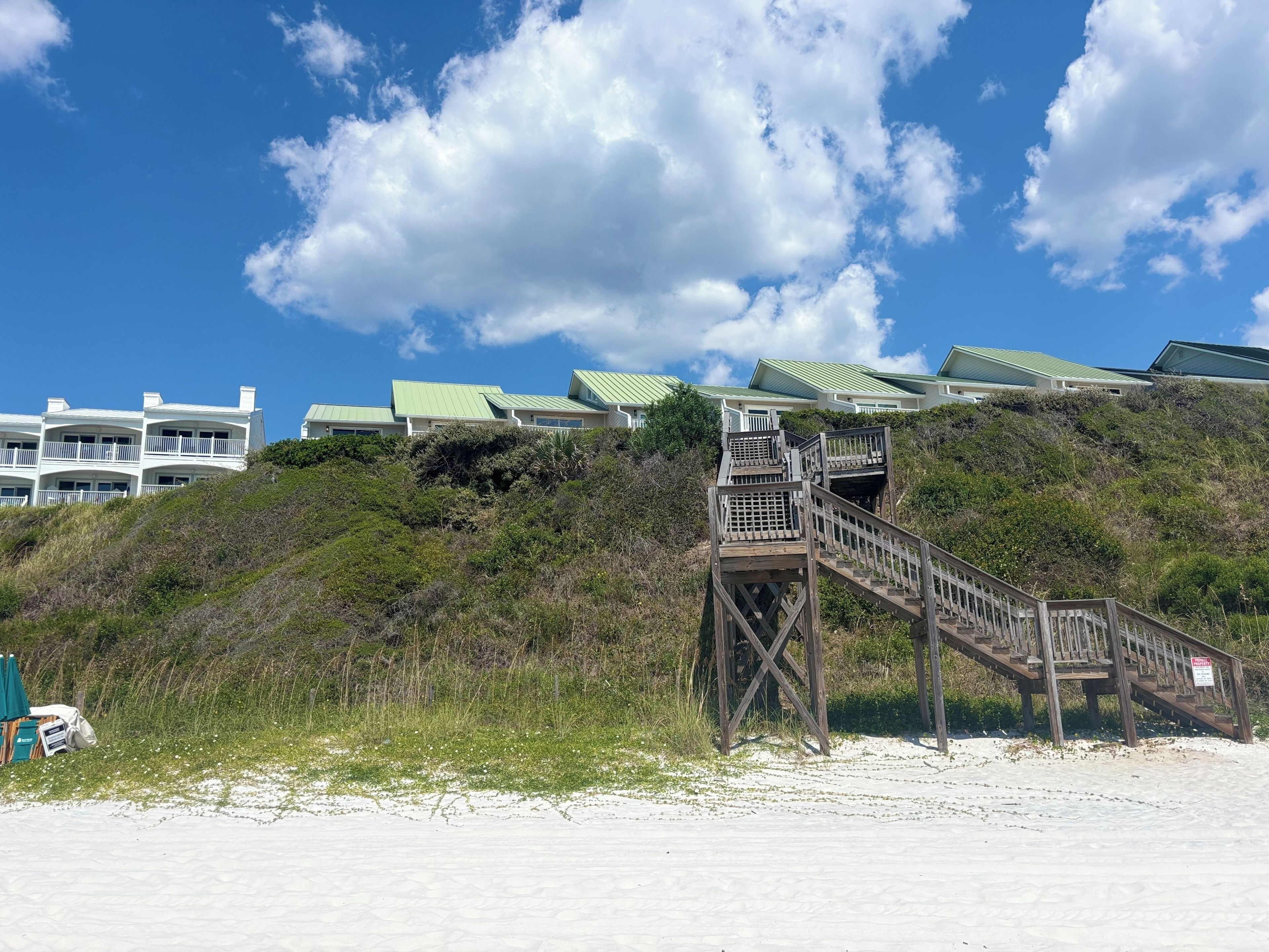 A beachfront property with a wooden staircase leading to a building with green roofs.