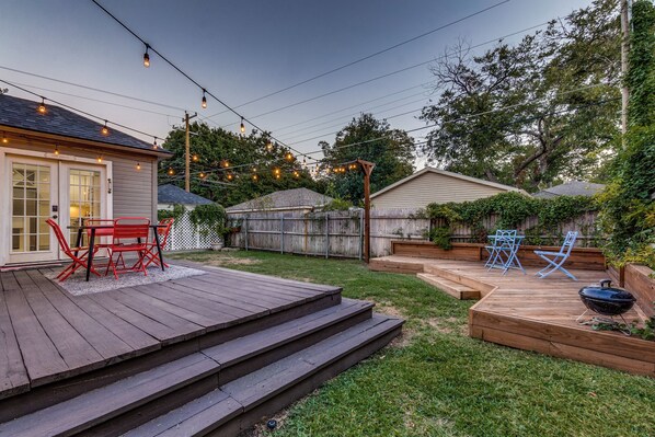 Un jardin avec une terrasse en bois, du mobilier d’extérieur et un barbecue.