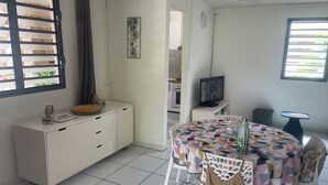A modern kitchen with white cabinetry, a dining area with a colorful tablecloth, and a television on a stand. - Country house 20 min from the beach (Rivière-Pilote)