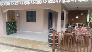 A covered outdoor seating area with a wooden fence, a stone-tiled floor, and a decorative wall. - Country house 20 min from the beach (Rivière-Pilote)