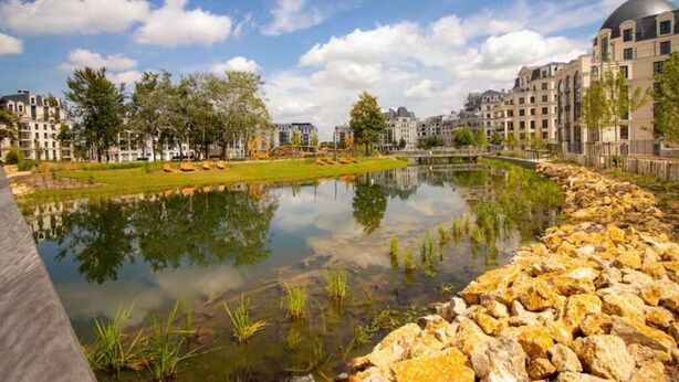Um parque urbano tranquilo com um lago, refletindo edifícios e árvores.