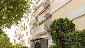 Edifício residencial com vários andares, varandas, entrada de vidro e vegetação ao redor.