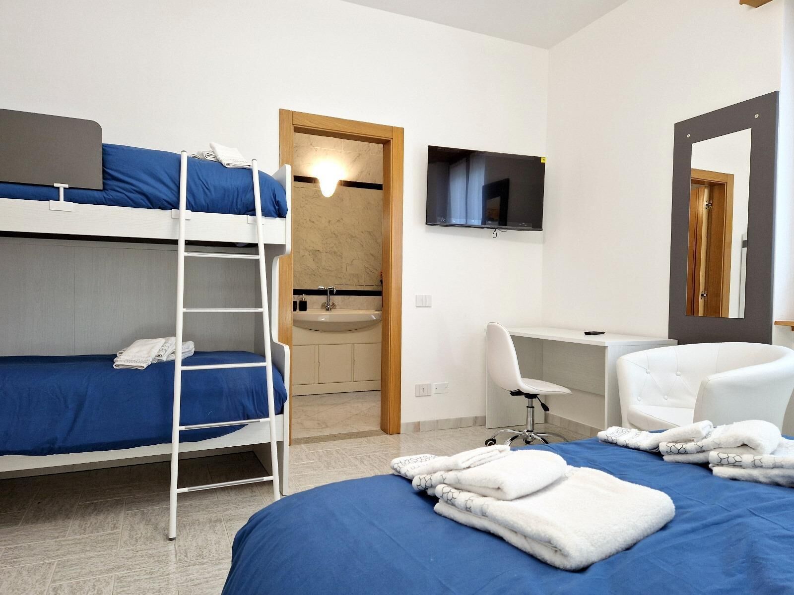 A hotel room with a bunk bed, a desk, a chair, a TV, and a bathroom.