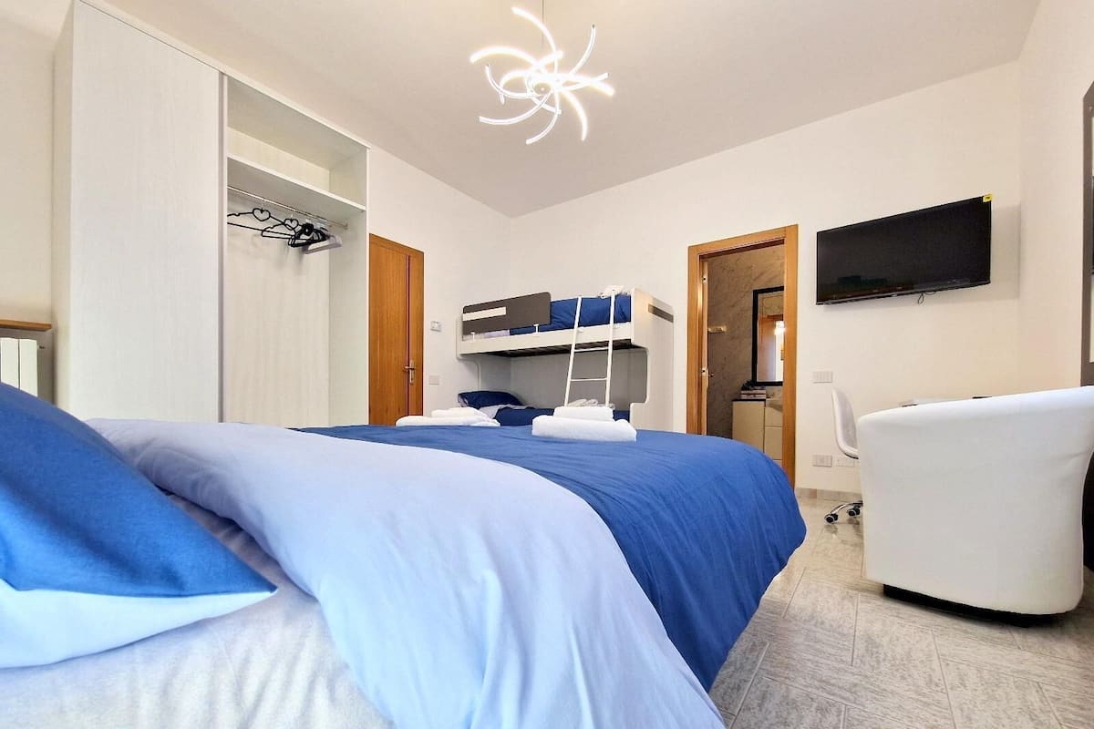A hotel room with a bunk bed, a desk, a chair, a TV, and a wardrobe.
