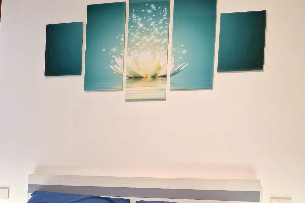 A neatly made bed with blue bedding and a rolled-up towel, a wall with a large floral artwork, and a white headboard.