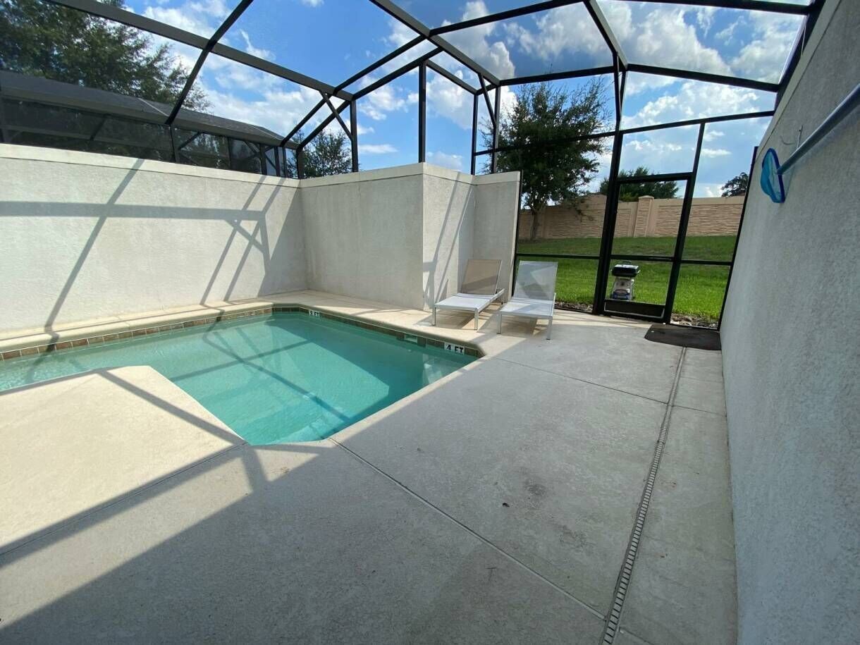 Une piscine extérieure couverte, offrant une vue dégagée sur le ciel, entourée d’une terrasse en béton et d’une clôture en métal.