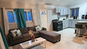 A modern living room with a sectional sofa, a coffee table, and a kitchen area with cabinets and appliances. - Queen's Court 2-bedroom apartment in Nassau! (Nassau)