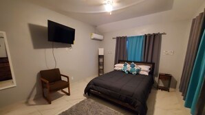 A bedroom with a bed, a chair, a TV, and an air conditioning unit. - Queen's Court 2-bedroom apartment in Nassau! (Nassau)