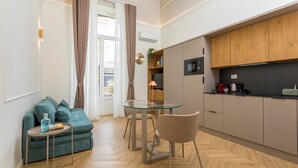Ein kompakter Wohnbereich mit einer Couch, einem Esstisch mit Glasplatte, einer Küchenzeile mit Holzschränken und einem Parkettboden.